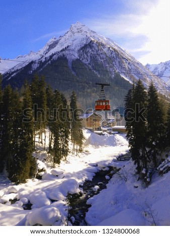 Old cabin for skiers and snowboarders in the mountains Dombay, Caucasus, Russia. Retro gondola. Landscape with a mountain river, mountains, the sun, houses and a red lift. Mobile photo.
