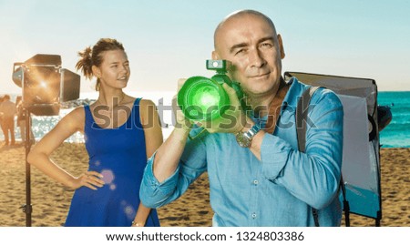 Portrait of cheerful positive  male photographer with camera among professional photo equipment on seaside