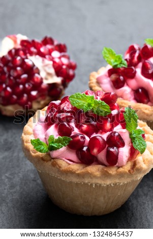 Mini  tarts with pink cream and pomegranate seeds on black stone background 
