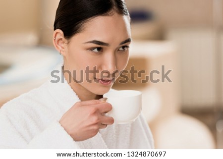 attractive asian woman in bathrobe drinking coffee at spa 