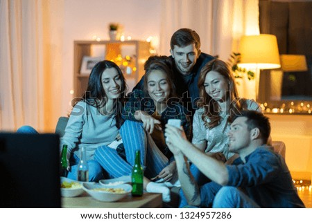 friendship, people, technology and entertainment concept - happy friends with smartphone, snacks and non-alcoholic drinks watching tv at home in evening