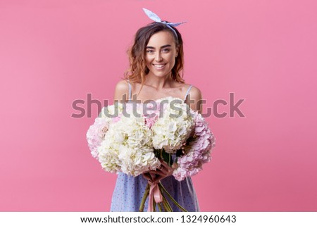 Cheerful young lady with long brown hair being excited to get bouquet of spring flowers on women's day isolated over pink background.