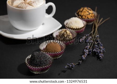 Chocolate Sweets Covered with Peanuts, Cocoa, Poppy Seeds, Candy Stars, Coconut Chips. Handmade Candies and Cup of Coffee with Marshmallow on Dark Background. Tasty Luxury Dessert
