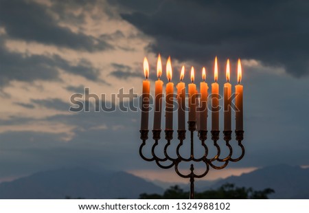 Menorah with burning candles  - traditional candelabra for Hebrew Holiday. Photo was taken against the colorful background of cloudscape at sunrise, selective focus applied
