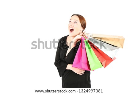Excited young woman looking up while holding different color shopping bags against a white background