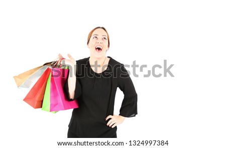 Excited young woman looking up while holding different color shopping bags against a white background