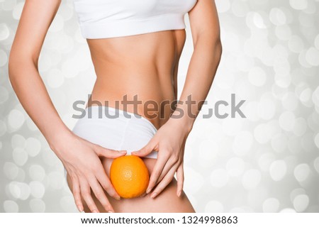 Female slender body in sport underwear holding orange on sea background
