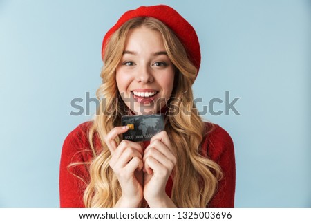 Photo of charming blond woman 20s wearing red beret holding credit card isolated over blue background in studio
