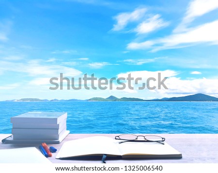 Sea, blue sky and white clouds. Nature, On the desk consists of tablet, glasses, diary, pen Huge pile of books and Writing notebook to record their memories., in Pattaya, Thailand.
