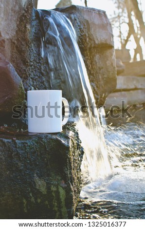 A solo blank tea mug on the edge of the rocks on the waterfall in the cold park pond. 