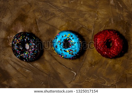 Overhead picture of three donuts of different colors, red, blue and dark brown, over brown background
