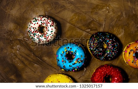 Overhead picture of group of colored donuts, over brown background
