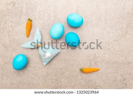 Easter bunny (rabbit) paper gift egg wrapping with knitted carrots idea. Handicraft (homemade) concept for children (kids). On stone background, top view.