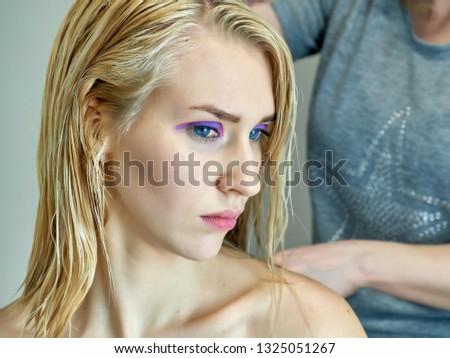Concept work of a beautician cosmetologist in with office. Makes hair, applies makeup on a gray background. Paints eyes, lips, hair with a blonde model brush. Photo portrait close-up.