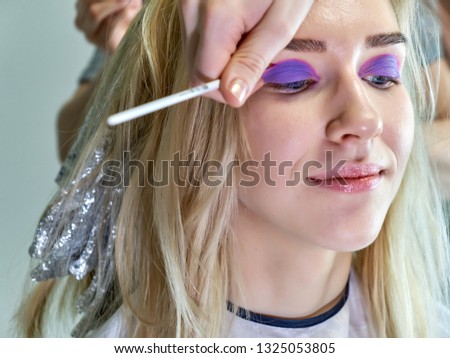 Concept work of a beautician cosmetologist in with office. Makes hair, applies makeup on a gray background. Paints eyes, lips, hair with a blonde model brush. Photo portrait close-up.
