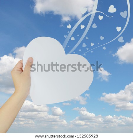 hand holding paper heart on blue sky background