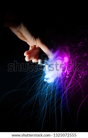 Male hand holds vape upside down. Vape clouds splash from coil on black background. Fog is two-colour blue and purple. Stock isolated dual color smoke with spray boiling glycerine.