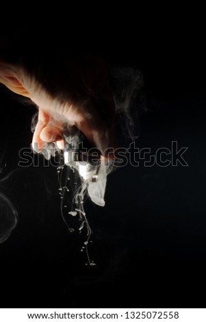 Male hand holds vape upside down. Vape clouds splash from coil. Fog is white. Stock isolated white smoke with spray boiling glycerine on black ground.