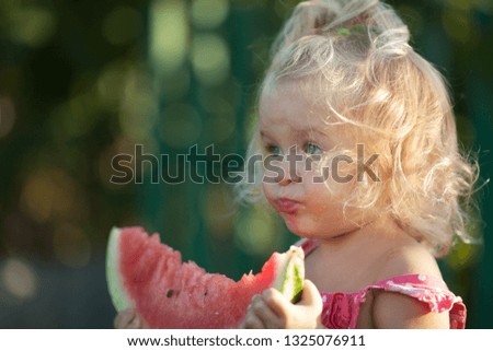 Happy little girl is eating watermelon in summer garden, outdoor.