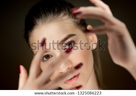 Portrait of young beautiful brown-haired girl with natural makeup holding her fingers in front of her face