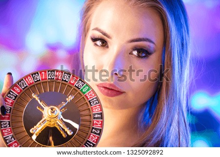 Casino concept. Portrait of young attractive woman, playing in casino. Poker chips, cards, roulette wheel, bokeh background.