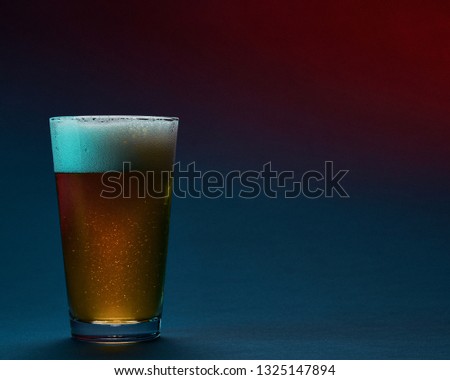Beer in a pint glass on a blue background with colored light.