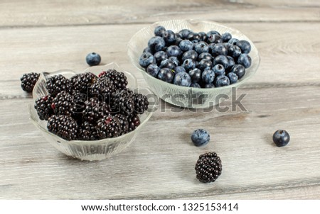 Small glass bowl of blueberries and blackberries on gray wood desk