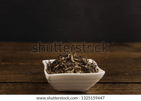 dry green tea in a white bowl isolated on wooden table on black background