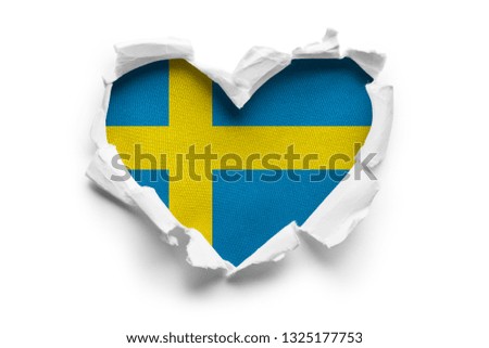 Heart shaped hole torn through paper, showing satin texture of flag of Sweden. Isolated on white background