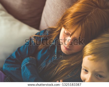 Two blonde sibling kids in blue shirts on a sofa watching something