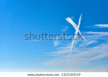White clouds as an x shape sign against a saturated blue sky with copy space on the left      