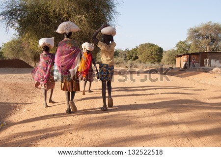 African Pokot girls leave the market in Amudat, Karamoja, carrying bags with food. Uganda, Africa. Royalty-Free Stock Photo #132522518