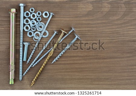 Several various metal fasteners for construction. Self-tapping screw screws, bolt, anker, nuts, washers and washer-grover, close-up on a wooden background.
