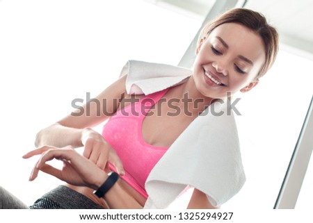 Young woman wearing towel around neck in gym healthy lifestyle sitting near window checking time on digital watch smiling cheerful