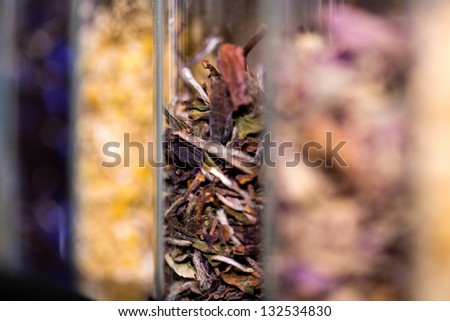 Glass container in focus half filled with herbs.