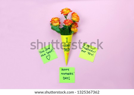 I love mom. Mother's day. Note reminder yellow sticker and beautiful fresh vivid orange roses tinged with red in yellow paper bag on pink background. LOVE MOM message