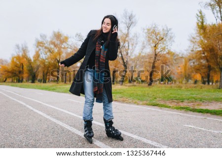Young beautiful smiling girl in casual wear roller skating listens to music. Autumn walk in the fresh air.