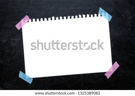 Empty paper sheet with white texture and pink, blue masking tape on black chalkboard surface. Copy space for add text or art work designs.