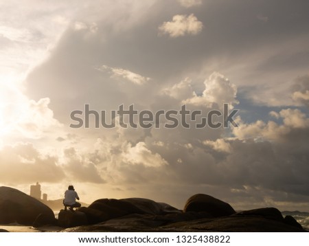 Male tourists Sitting down on the rocks to take pictures of the beautiful atmosphere of the sea in the morning