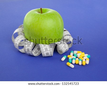 Picture of apple,  tape measure and pills on the blue background