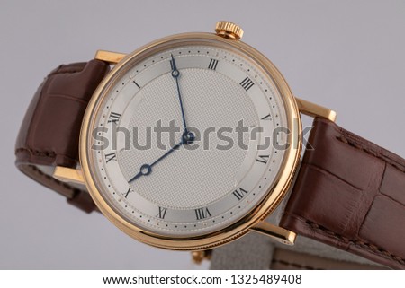 Men's watch with brown leather strap,white dial, in golden body,blue clockwise,black numerals isolated on gray background. 