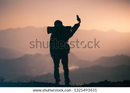 Silhouette of young tourist with backpack standing take photo on the mountain. travel concept.