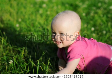 Cute smiling little baby in pink dress crawling in the green meadow on a sunny summer day