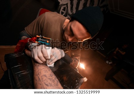 A man master fills a tattoo to a young man. Tattoo parlor. Drawing on skin. Lifestyle