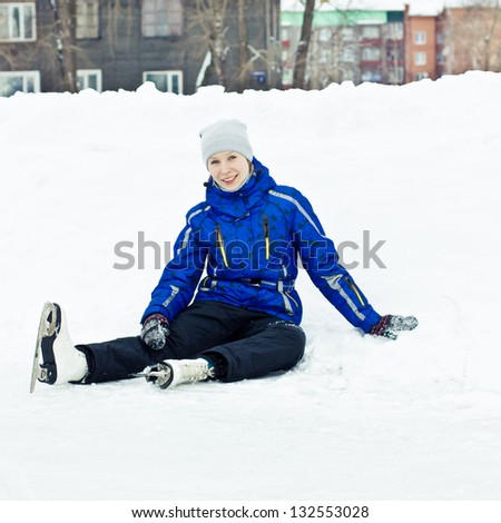 Woman in skates sitting on the ice smiling.