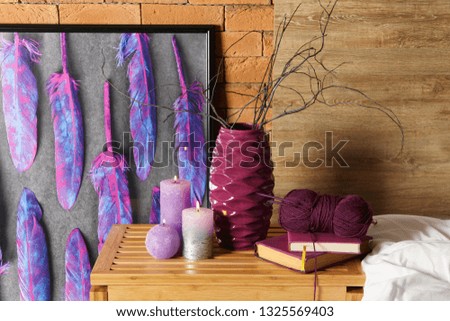 Burning candles with books and knitting yarn on wooden table in bedroom