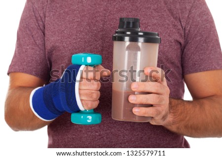 Close up picture of a young man holding a dumbbell and a shake