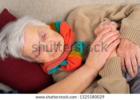 Close up picture of sick elderly woman resting on the sofa, caregivers hand holding her hands - seasonal influenza