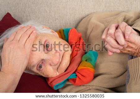 Close up picture of sick elderly woman with fever resting on the sofa, caregivers hands holding her
