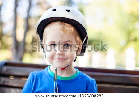 Little blonde boy 3 years old in white sport helmet and blue t-shirt outside. Special problems with kid's eyes. Myopie, astigmatism, cross-eyed. Royalty-Free Stock Photo #1325608283